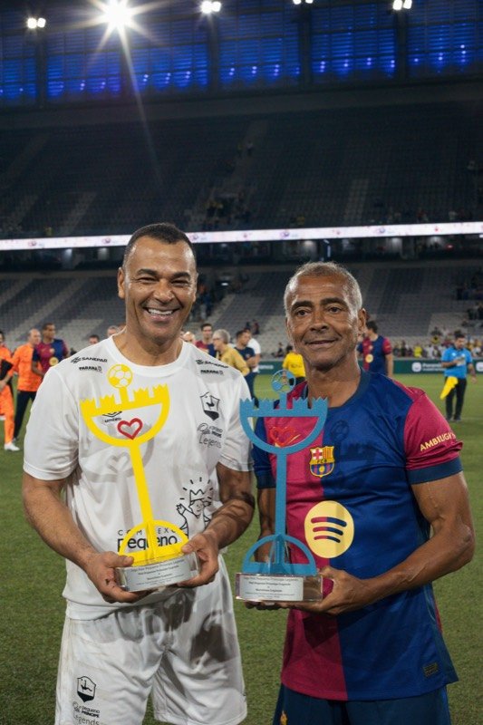 Cafu e Romário com troféus no gramado, no jogo comemorativo